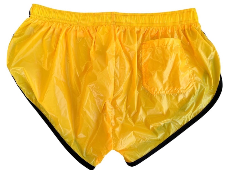 Op de afbeelding: Felge gele sportbroek met zwarte rand. De shorts hebben een klein zakje aan de achterkant en een elastische tailleband. Het materiaal lijkt glanzend, lichtgewicht nylon.