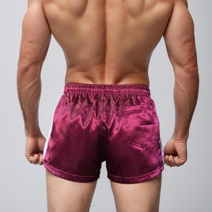 Puede incluir: Pantalones cortos deportivos de sat&eacute;n burdeos con rayas laterales blancas. Los pantalones cortos tienen un bolsillo trasero y una cintura el&aacute;stica. Los pantalones cortos se muestran desde la espalda.