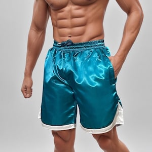 May include: Teal satin shorts with a drawstring waist and white trim. These athletic shorts have a shiny, smooth texture and a relaxed fit. The shorts are designed for comfort and style.