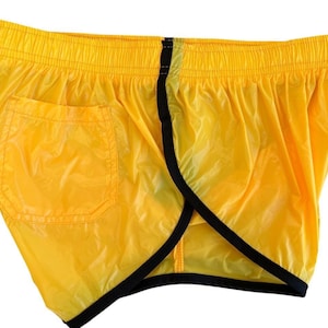 Op de afbeelding: Felge gele sportbroek met zwarte rand en &eacute;&eacute;n zak. De shorts hebben een elastische tailleband en zijn gemaakt van een lichtgewicht, enigszins transparant materiaal.