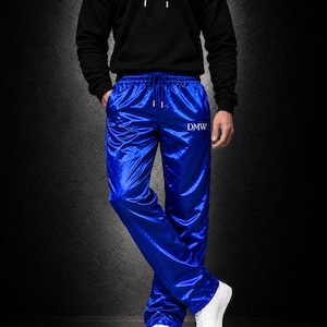 May include: Bright royal blue satin track pants featuring an elastic waistband with a drawstring and the text DMW embroidered in white on the upper left thigh. The pants have a straight-leg fit and a smooth, reflective finish.