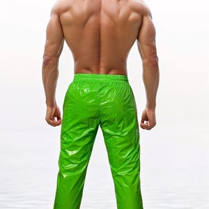 May include: Bright lime green pants with a glossy, reflective finish and an elasticized waistband. The pants feature a straight-leg cut and a smooth, synthetic-looking material that catches the light, creating distinct highlights and shadows.