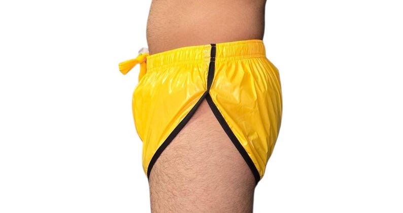 Op de afbeelding: Gele sportbroek met zwarte rand. De shorts hebben een trekkoord en een splitzoom. Het materiaal lijkt een glanzende, lichtgewicht stof te zijn. De shorts worden van opzij getoond.