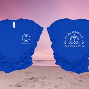 Puede incluir: Dos camisetas azul real con texto y gr&aacute;ficos blancos. La camiseta delantera tiene un ancla y el texto "Captain Ryan". La camiseta trasera tiene un crucero, anclas y el texto "Cruising Together Bahamas 2024".