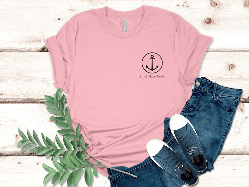Puede incluir: Una camiseta rosa con un dise&ntilde;o de ancla negra y el texto "First Mate Kelly" en la parte delantera.