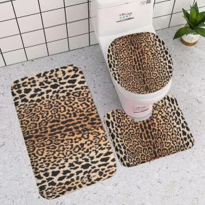 May include: A three-piece bathroom set featuring a toilet seat cover, a U-shaped contour rug, and a rectangular bath mat. Each piece displays a consistent brown, tan, and black leopard print pattern across the entire surface of the items.