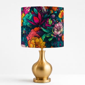 May include: A table lamp with a gold-colored base and a floral patterned lampshade. The lampshade features a dark background with vibrant flowers in shades of pink, yellow, orange, and teal. The lamp is a decorative lighting fixture.