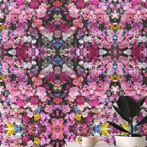 May include: A vibrant floral wallpaper design featuring a dense arrangement of pink, purple, white, and yellow roses and other flowers. The pattern is symmetrical, creating a visually striking and artistic display. A potted plant and books are in the foreground.