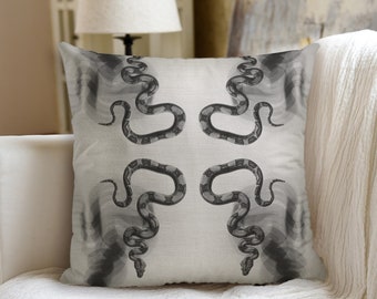 May include: A white throw pillow with a black and white snake pattern. The snakes are arranged in a symmetrical pattern, with their heads facing each other.