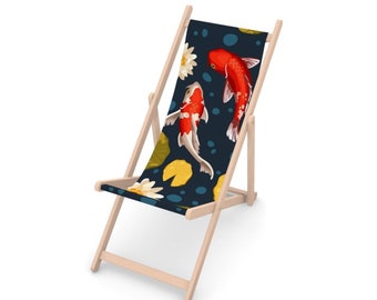 Puede incluir: Una silla de playa de madera con un tejido estampado en azul y blanco con peces koi rojos y blancos y nenúfares. La silla está plegada y tiene un acabado de madera natural.