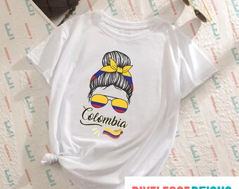 May include: White t-shirt with a graphic of a woman with a bun in her hair wearing sunglasses with the Colombian flag colors. The text "Colombia" is written below the graphic with a small Colombian flag.
