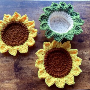 May include: Three crocheted sunflower coasters. Two are yellow with brown centers and one is green with a white center.