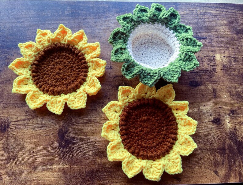 May include: Three crocheted sunflower coasters. Two are yellow with brown centers and one is green with a white center.