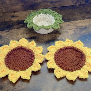May include: Two crocheted sunflower coasters with brown centers and yellow petals. A crocheted green and white bowl is also in the image.