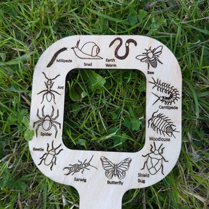 May include: Wooden cutout of a magnifying glass with various insects and other small creatures, including a spider, beetle, butterfly, centipede, and earthworm. The text on the cutout includes the names of each creature.