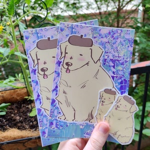 May include: Three stickers featuring a cartoon golden retriever wearing a brown hat. The stickers are on a purple and blue background with a watercolor effect. The stickers are different sizes.