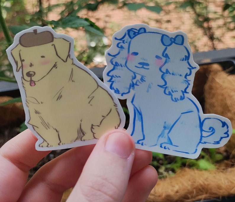 May include: Two illustrated dog stickers. One is a yellow dog wearing a brown hat. The other is a blue dog with a blue bow.