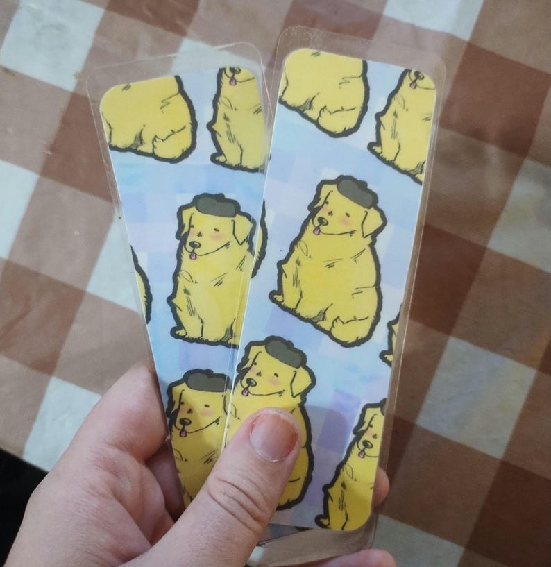 May include: Two clear plastic bookmarks with a repeating pattern of yellow dogs wearing black berets on a light blue background.