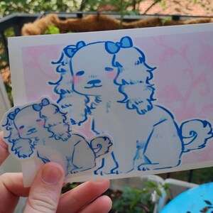 May include: Two white dogs with blue bows on their heads are drawn on a pink background. The larger dog is standing and the smaller dog is sitting. Both dogs have blue eyes and pink cheeks.