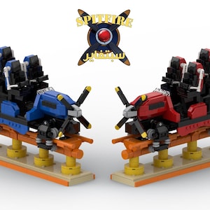 May include: Two toy roller coaster cars, one blue and one red, with black seating and propeller details. The cars sit on an orange track with yellow supports, and the word "Spitfire" is above them.