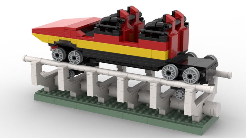 May include: A red and yellow Lego roller coaster car with black seats and wheels, on a white and grey track with green base plates.