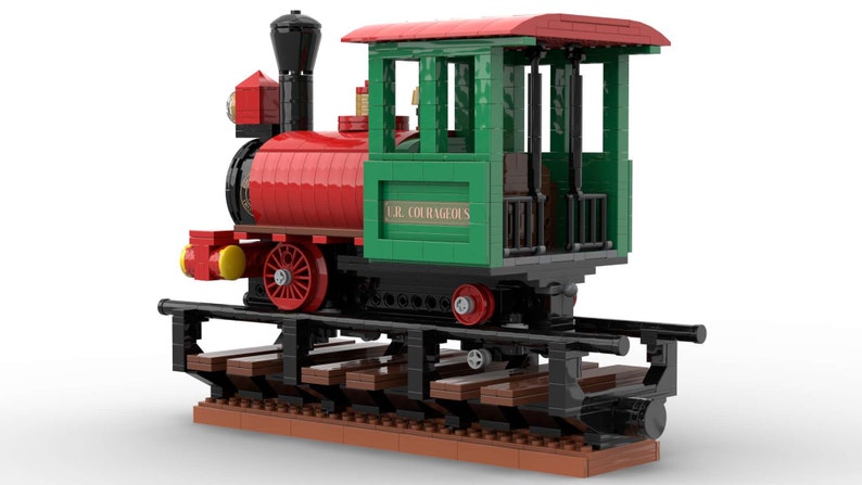 May include: A red and green toy train engine with a black chimney and wheels. The engine has a green cab with a sign that reads "C.R. COURAGEOUS". The train is on a track made of brown and black LEGO bricks.