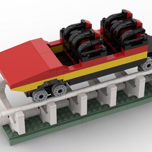 May include: A red, yellow and black Lego roller coaster car with black wheels and a white track. The car is on a green base with white supports.