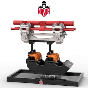 May include: A model of a roller coaster ride, constructed from interlocking toy bricks. The coaster features a red track, white supports, and a black car with orange engine details. The model sits on a black base, with the word "NINJA" in red.