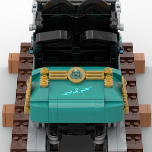 K&ouml;nnte beinhalten: Ein blaugr&uuml;ner und schwarzer Lego-Zug mit goldenen Akzenten. Der Zug hat einen goldenen Kopf mit einem Gesicht und die Worte "Tonnerre de Zeus" auf der Vorderseite. Der Zug befindet sich auf einem braunen Lego-Gleis.