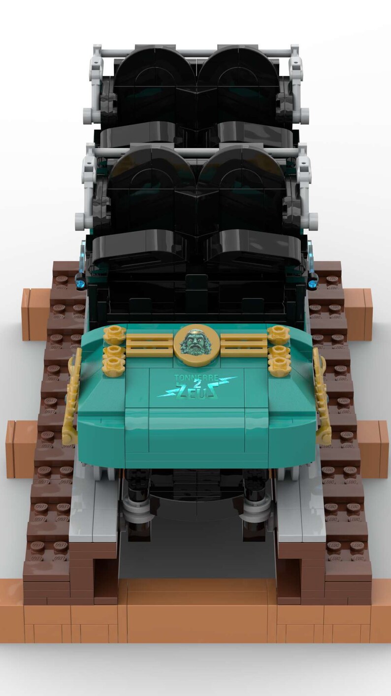 K&ouml;nnte beinhalten: Ein blaugr&uuml;ner und schwarzer Lego-Zug mit goldenen Akzenten. Der Zug hat einen goldenen Kopf mit einem Gesicht und die Worte "Tonnerre de Zeus" auf der Vorderseite. Der Zug befindet sich auf einem braunen Lego-Gleis.