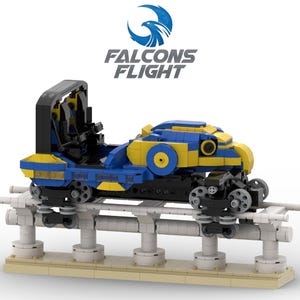 Puede incluir: Un modelo de vagón de montaña rusa en azul y amarillo, con el texto "Falcons Flight" arriba. El vagón está sobre una vía blanca sostenida por pilares blancos y una base beige. El vagón tiene ruedas negras.