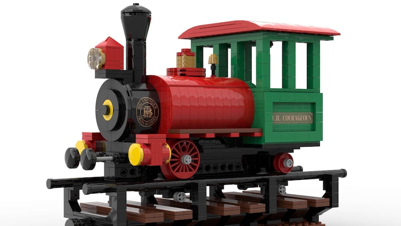 May include: A red and green Lego train engine with black wheels and a black smokestack. The engine has a yellow headlight and a sign that reads "The Little Red Caboose Railroad". The caboose is green and has a sign that reads "U.R. Courageous".