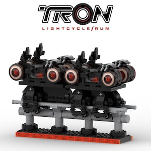 May include: A black LEGO model of the TRON Lightcycle Run ride. The model features multiple black vehicles with red accents and glowing red wheels, mounted on a gray track. The TRON logo is displayed above.