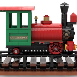May include: A red and green toy train with a black chimney and wheels. The train is on a track and has a sign that says "L.R. COURAGEOUS".