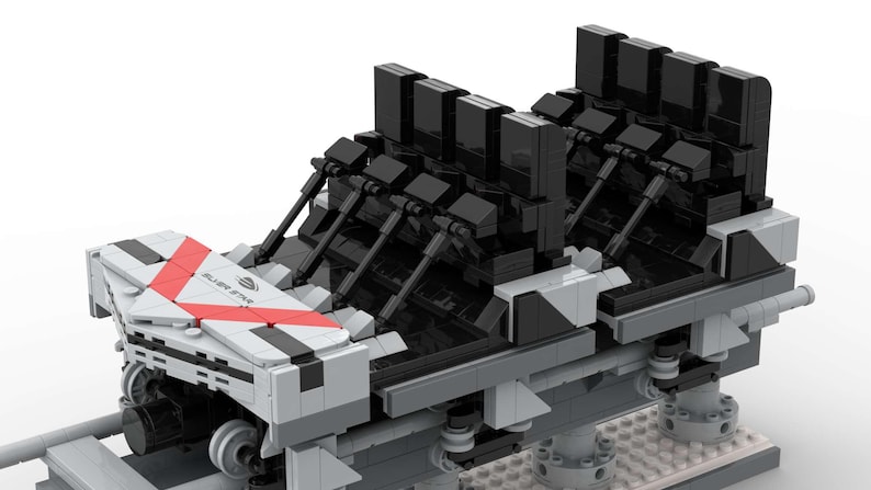 Pu&ograve; includere: Modello dettagliato di una carrozza di montagne russe, costruito con blocchi ad incastro. La carrozza presenta una combinazione di colori grigio e bianco con accenti rossi e sedili neri. Il modello include ruote e strutture di supporto, suggerendo ingegneria e design.