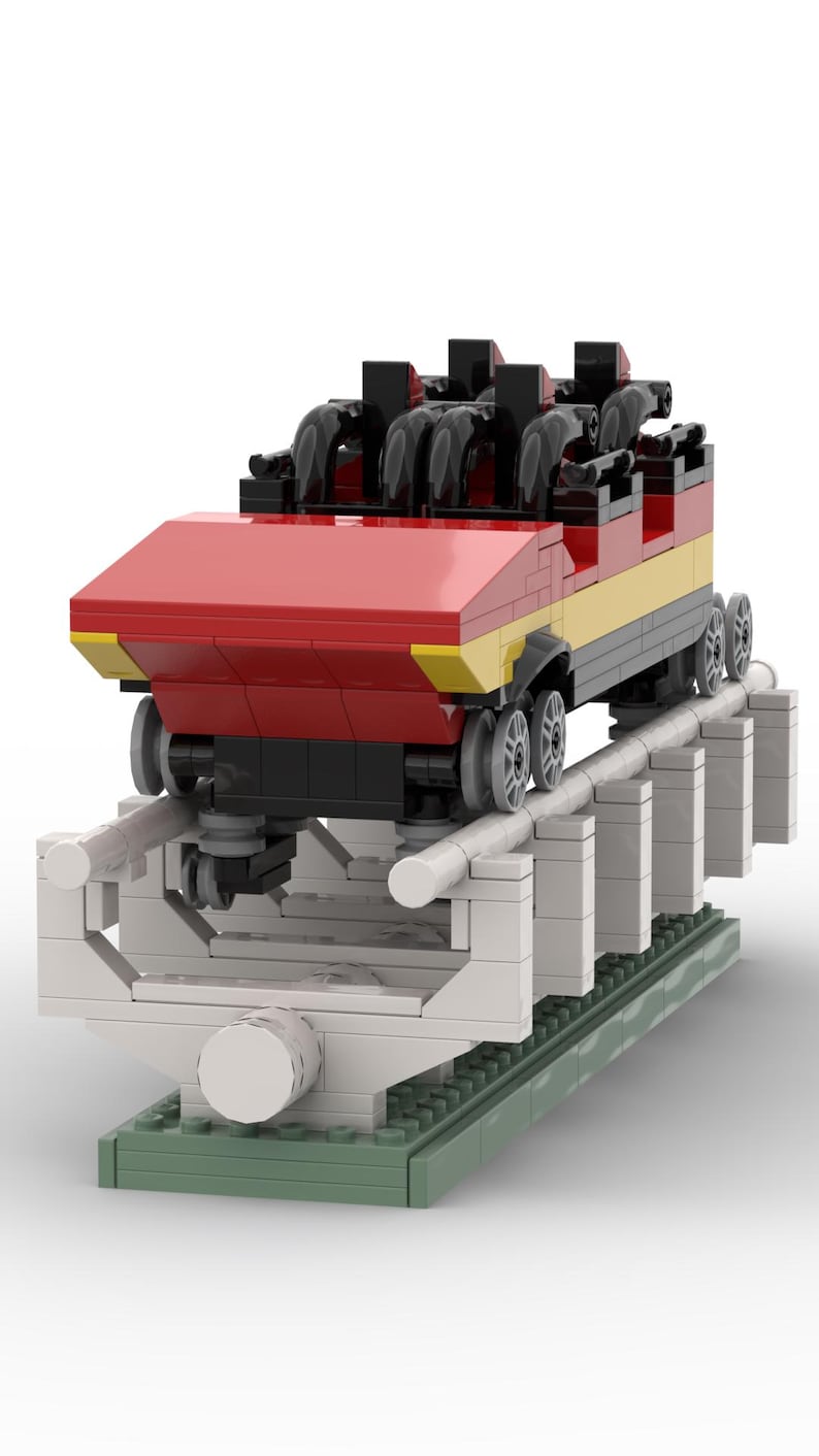 May include: A red and yellow Lego roller coaster car with black seats and wheels, on a white and grey track with green base plates.