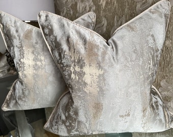 May include: Two decorative throw pillows with a light grey and gold metallic abstract pattern. The pillows are made of a soft, textured fabric.