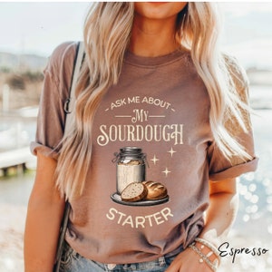 May include: A brown t-shirt with the text "Ask me about my sourdough starter" and a drawing of a jar of sourdough starter and bread.