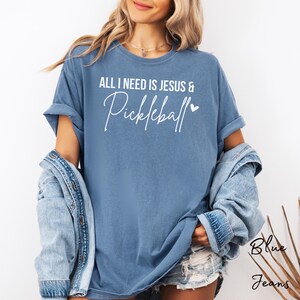 Puede incluir: Una camiseta azul con el texto "All I need is Jesus & Pickleball" en letras blancas con un peque&ntilde;o coraz&oacute;n.