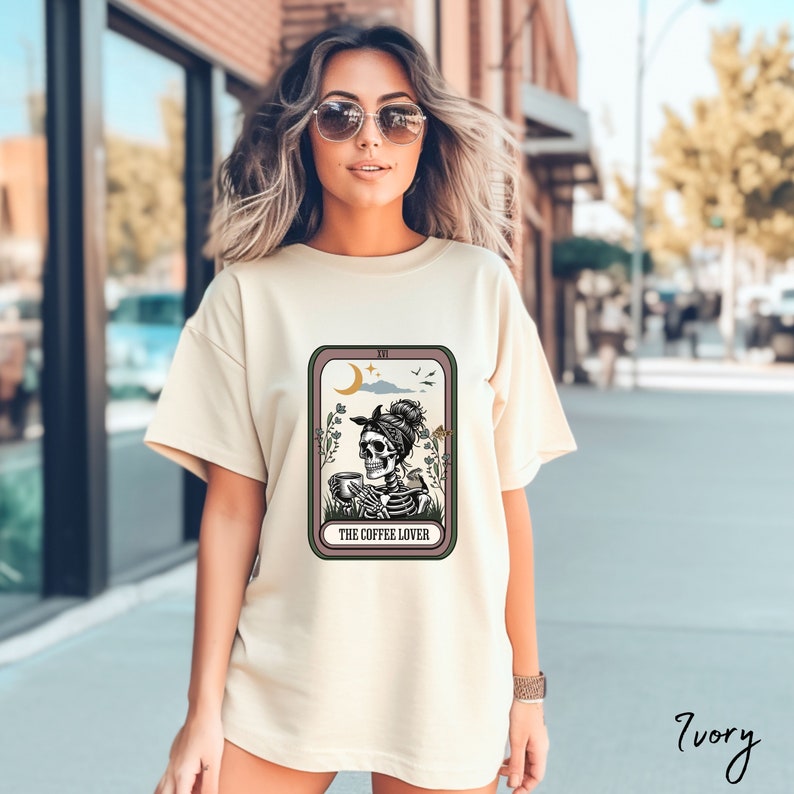 May include: A cream coloured t-shirt with a graphic of a skeleton drinking coffee. The graphic is in a tarot card style with the text "The Coffee Lover".