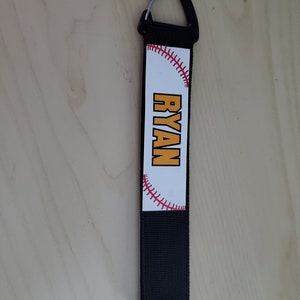 May include: Black and white baseball-themed keychain with a red stitch design and the name "RYAN" in yellow letters.