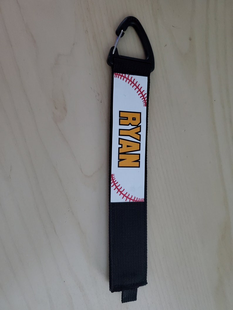 May include: Black and white baseball-themed keychain with a red stitch design and the name "RYAN" in yellow letters.