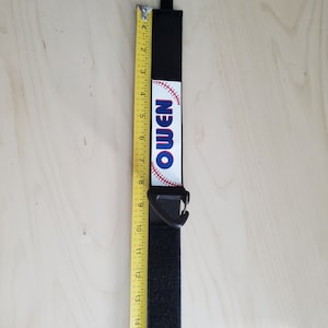 May include: Black velcro strap with a white baseball graphic and the word "Owen" printed on it. The strap has a black plastic clip.