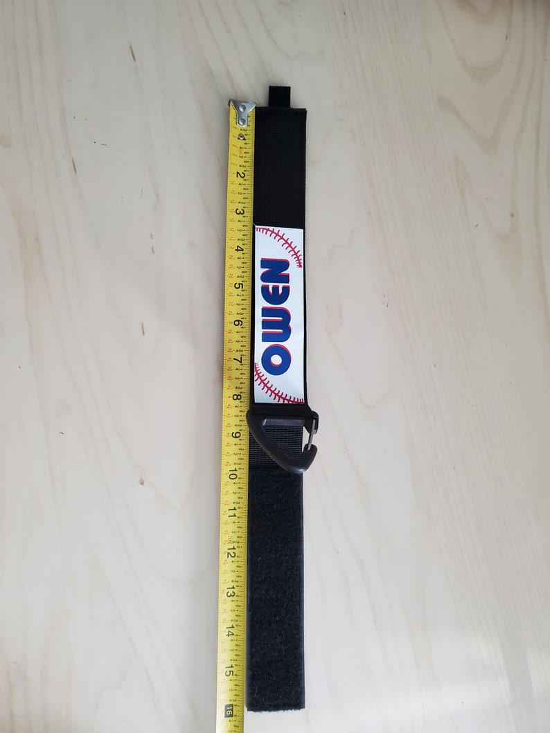 May include: Black velcro strap with a white baseball graphic and the word "Owen" printed on it. The strap has a black plastic clip.
