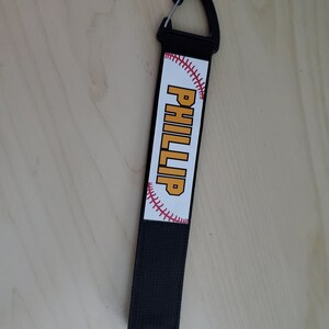 May include: Black baseball keychain with a white baseball graphic and the name "PHILLIP" in yellow text.