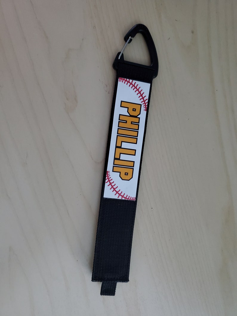 May include: Black baseball keychain with a white baseball graphic and the name "PHILLIP" in yellow text.