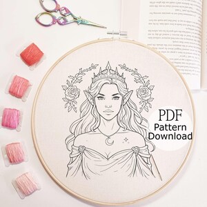 May include: An embroidery hoop with a detailed line drawing of a woman with pointed ears, a crown, and a crescent moon necklace. The text "PDF Pattern Download" is visible. Pink thread spools and rainbow scissors are also in the image.