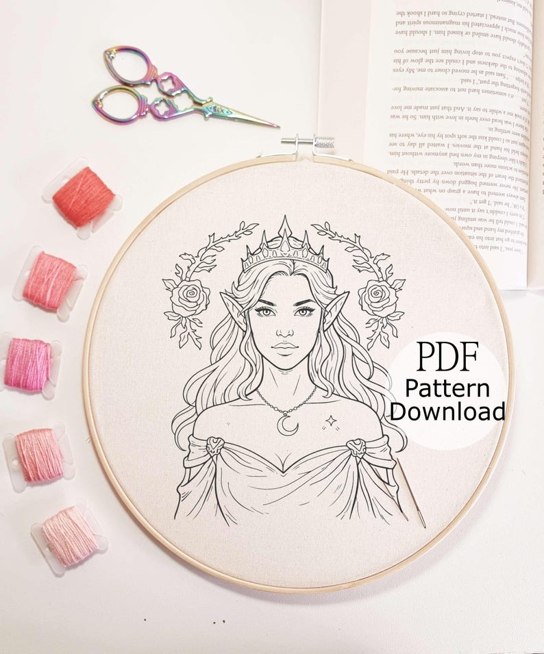 May include: An embroidery hoop with a detailed line drawing of a woman with pointed ears, a crown, and a crescent moon necklace. The text "PDF Pattern Download" is visible. Pink thread spools and rainbow scissors are also in the image.
