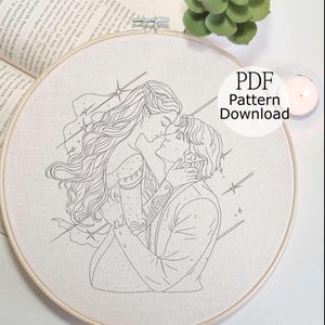May include: An embroidery hoop with a line art design of a couple embracing, with stars and lines radiating outward. The text "PDF Pattern Download" is visible. The hoop is set against a neutral background with a book and a succulent.