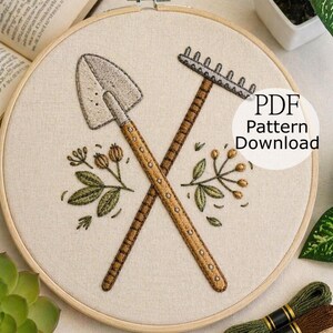 May include: Embroidery hoop featuring a crossed shovel and rake design, with floral accents. The tools are brown and beige, stitched on a cream-colored fabric. The text "PDF Pattern Download" is visible. The image also includes embroidery floss and a needle.